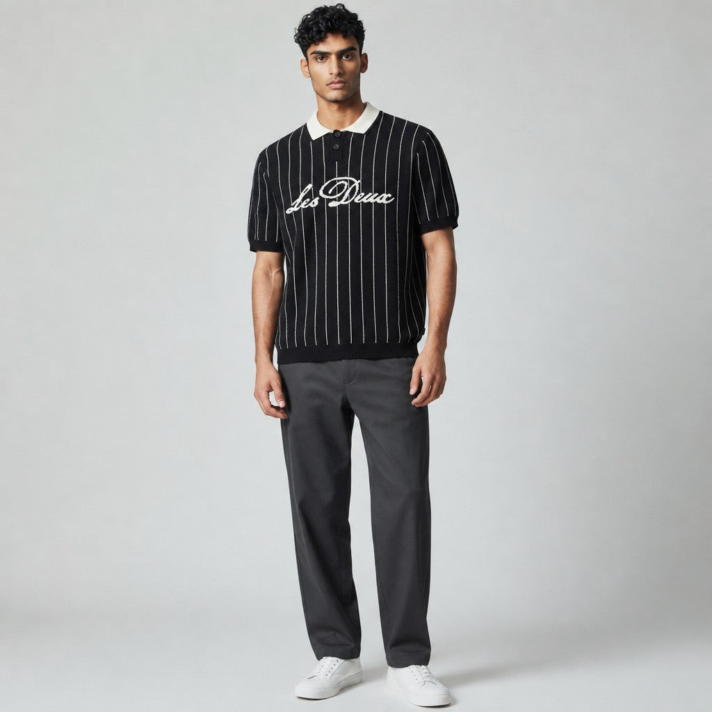 Modello indossa polo in maglia RBoutique nera a righe verticali bianche con colletto crema e logo ricamato sul petto